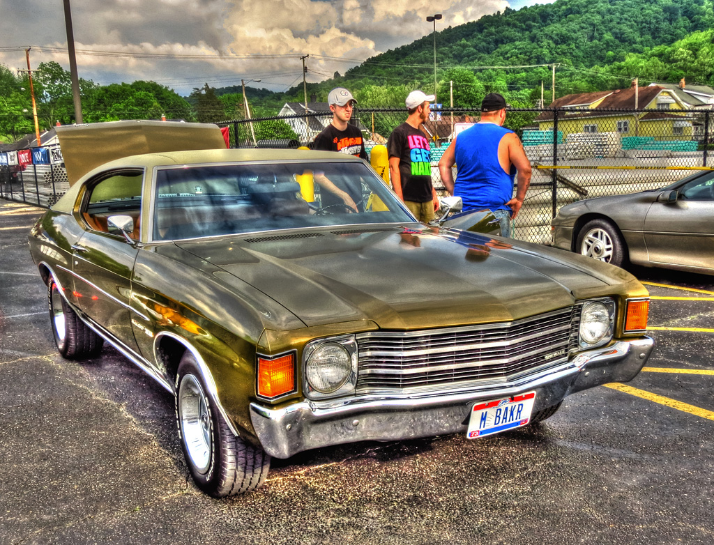 two guys standing next to an old fashioned car in a parking lot