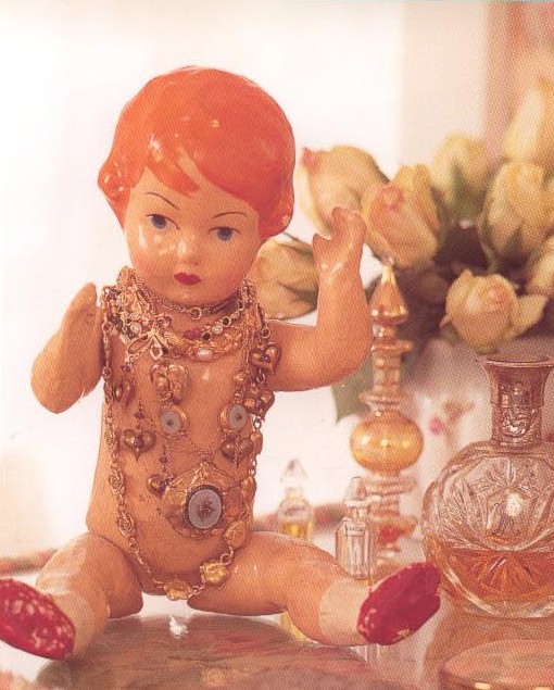 a doll next to a vase filled with flowers and some perfume bottles