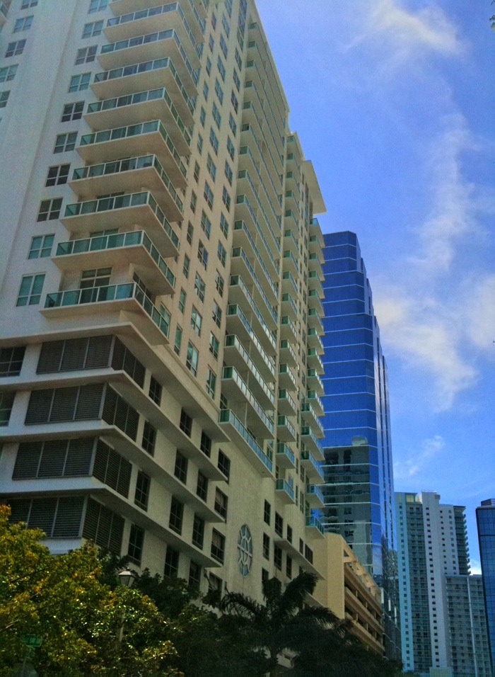 two tall buildings with trees near them under a blue cloudy sky