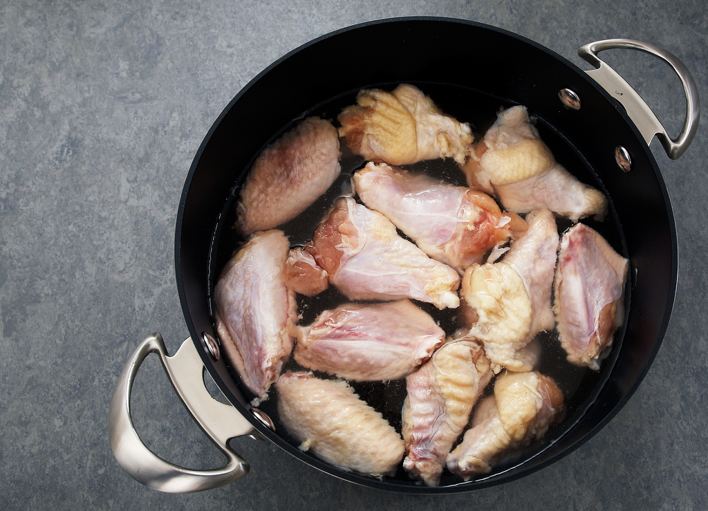 some raw chicken is sitting in a pot with some tongs