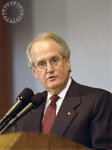 a man wearing glasses and a red tie standing in front of a microphone