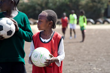 two girls holding soccer balls in the middle of a road