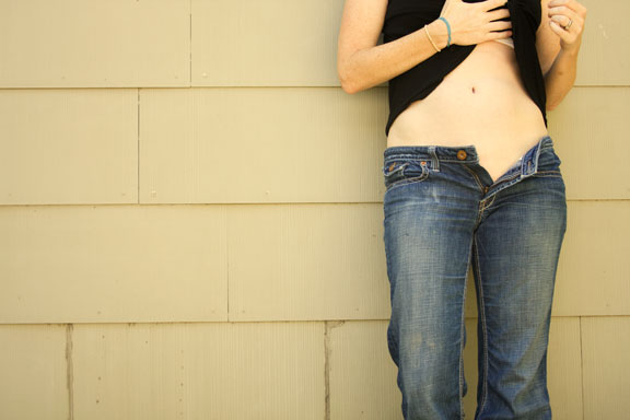 a woman in jeans and a black top leaning on a wall