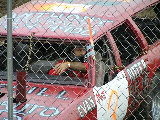 a man in a red car sitting behind chain link fence