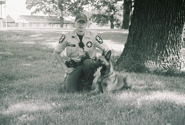 a man in a uniform sitting by a tree with his dog