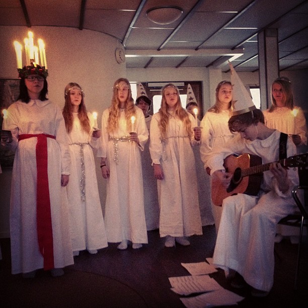 a group of women in white choir robes singing while holding lit candles
