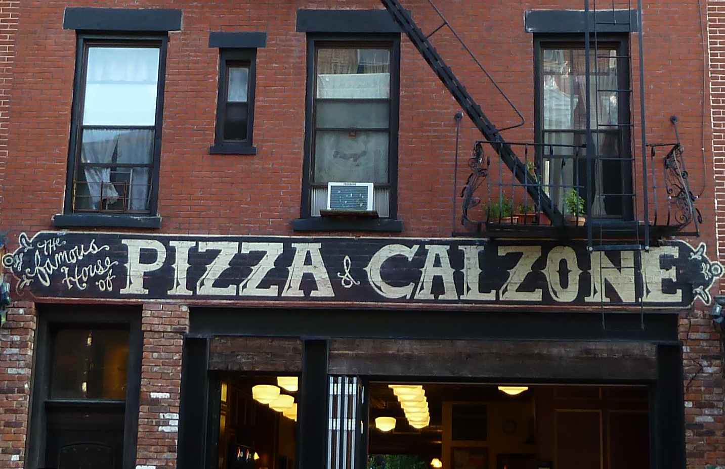 the large sign on the building says pizza & calzonee