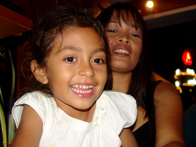 a child in a dress smiles as her mother watches