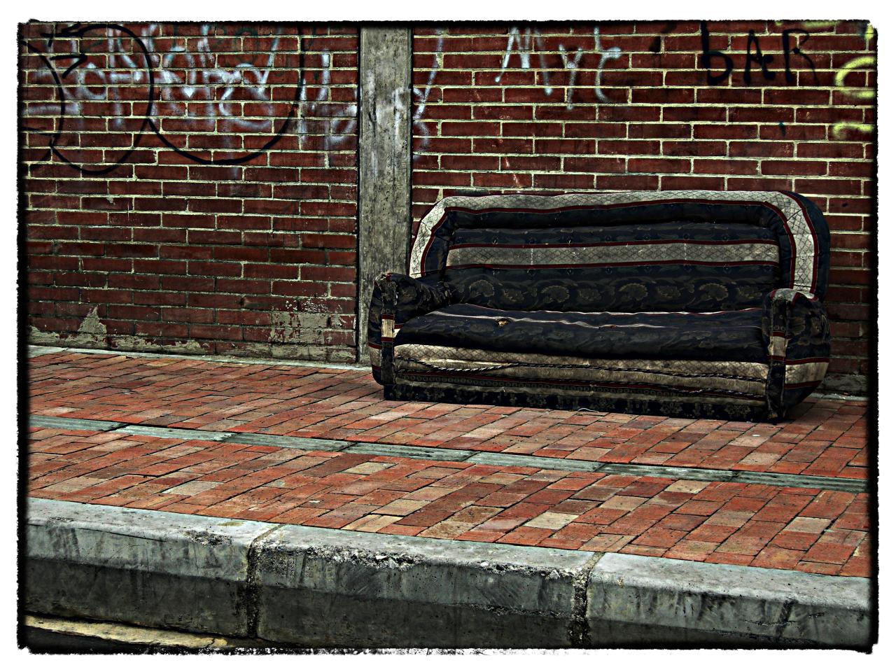 a bench on the sidewalk with graffiti writing behind it