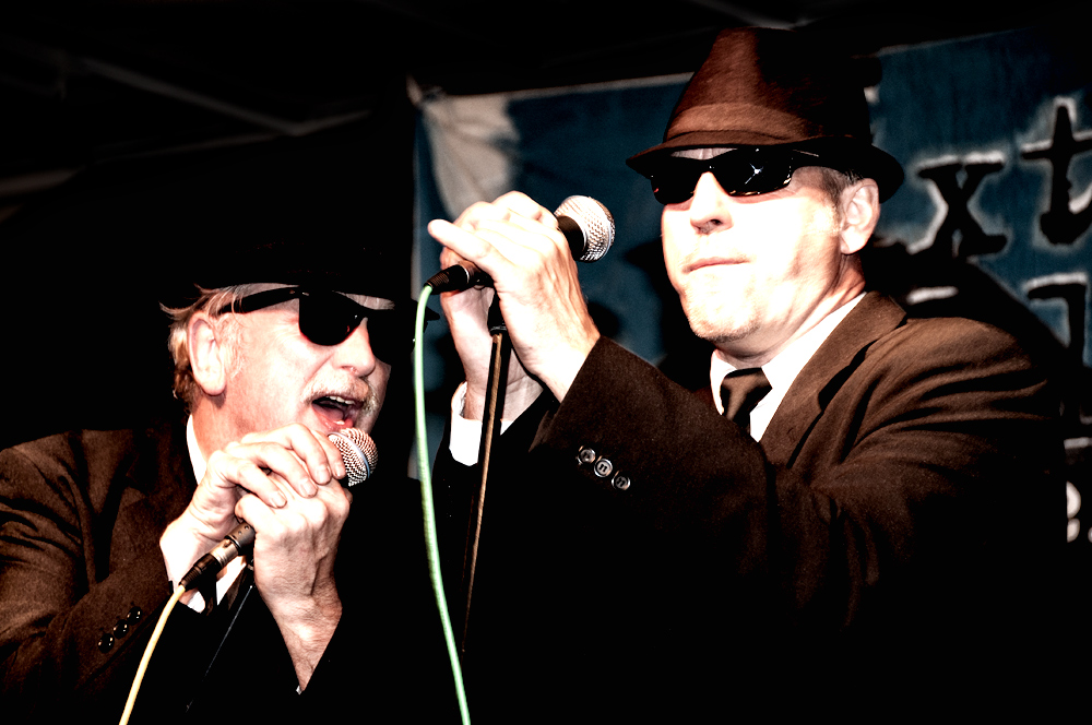 two men wearing suits and hats stand and sing