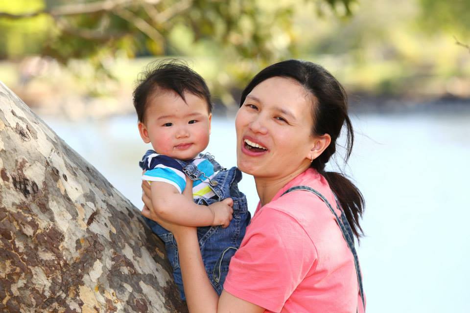 a young woman holding a baby next to a tree