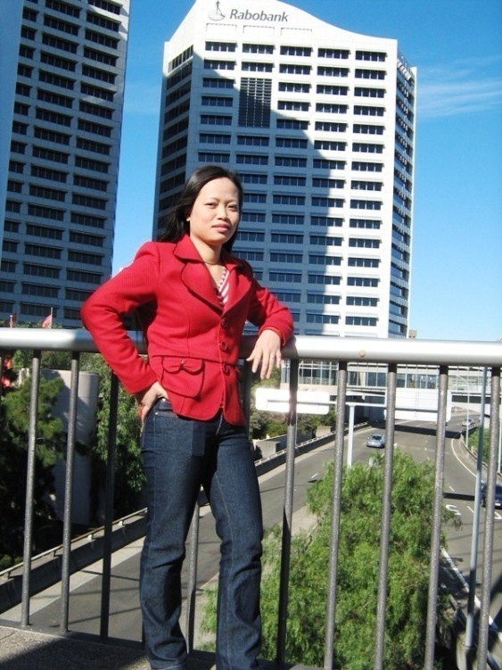 a lady in red is posing on a railing near some buildings