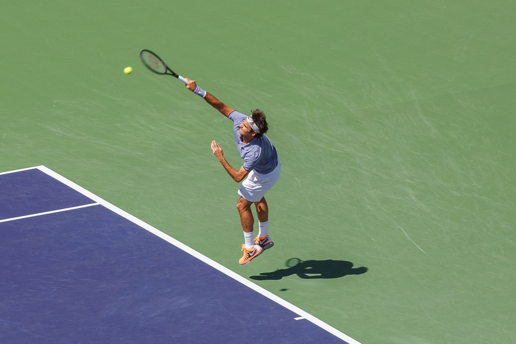 a tennis player wearing blue jumps as he hits the ball