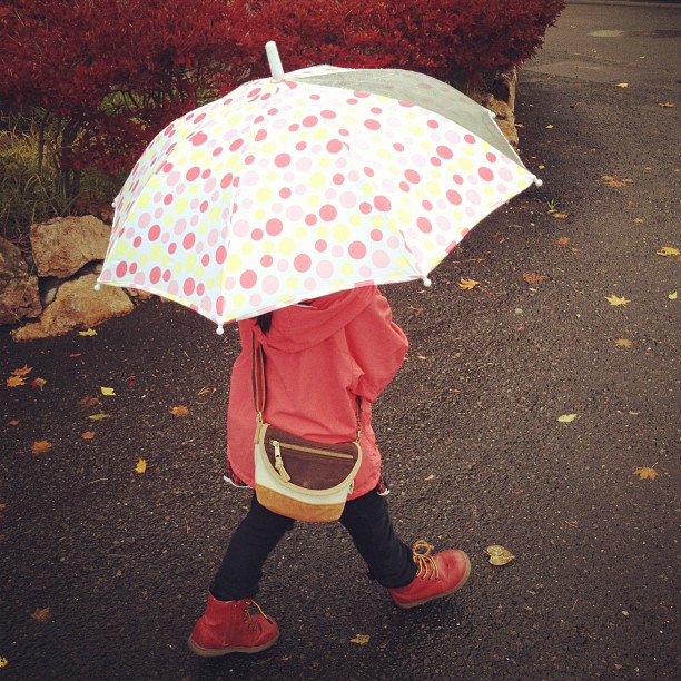 a child with an umbrella is walking on the sidewalk