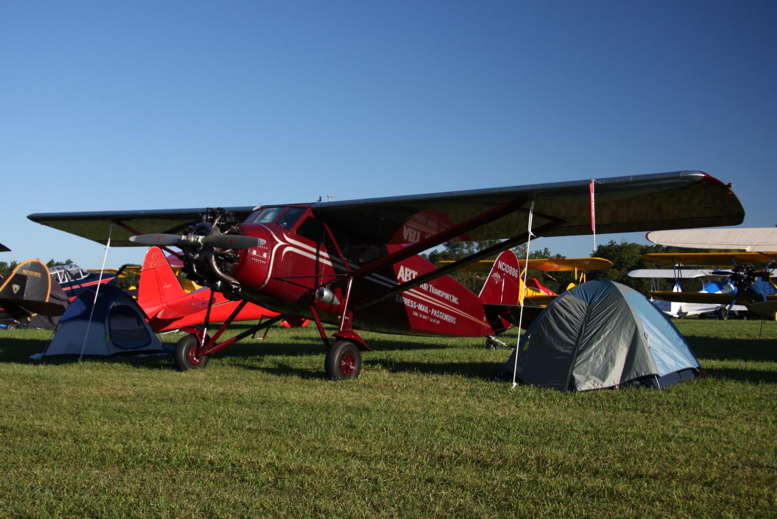 an old red airplane sits with two tents nearby