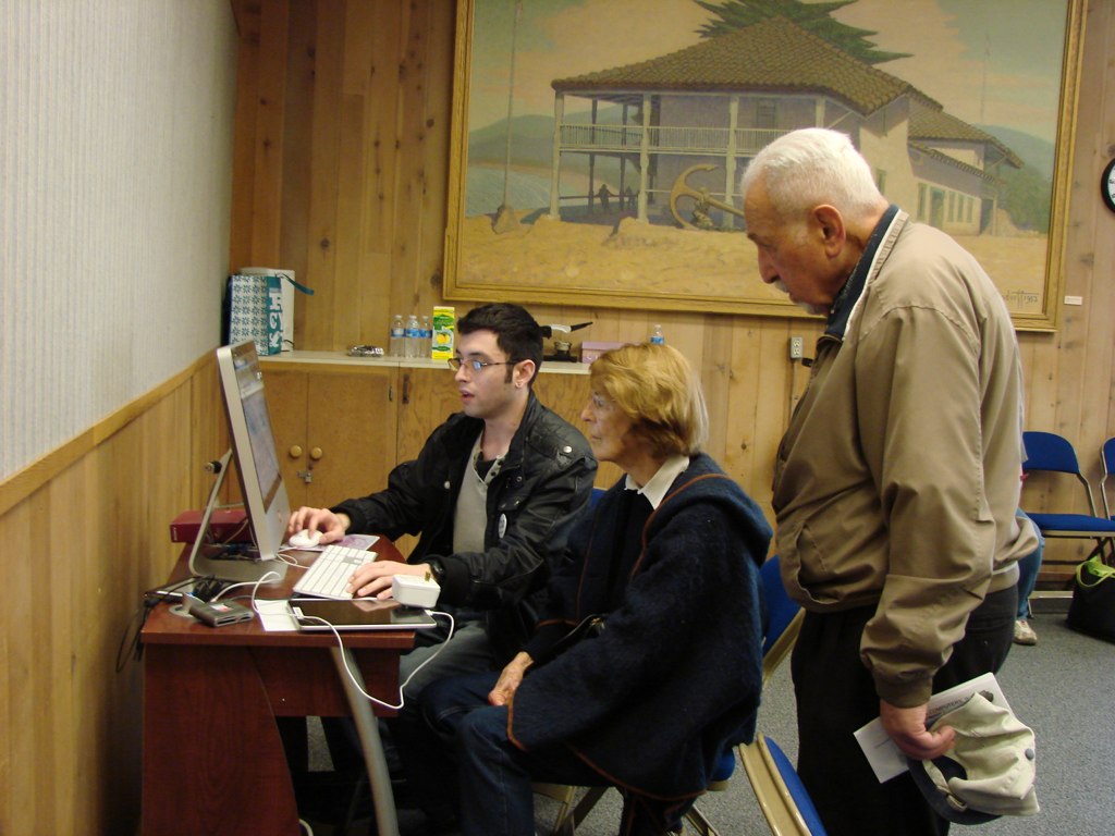 two adults sitting at a computer talking to one another