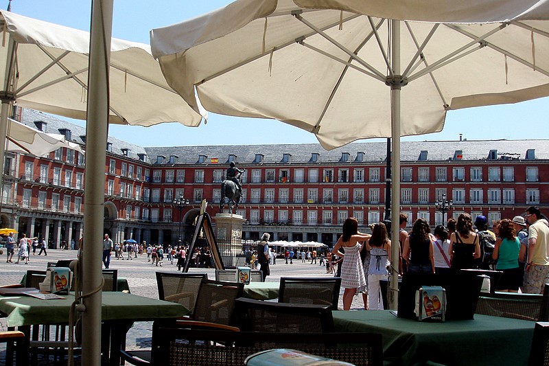 some tables that are with umbrellas near many people