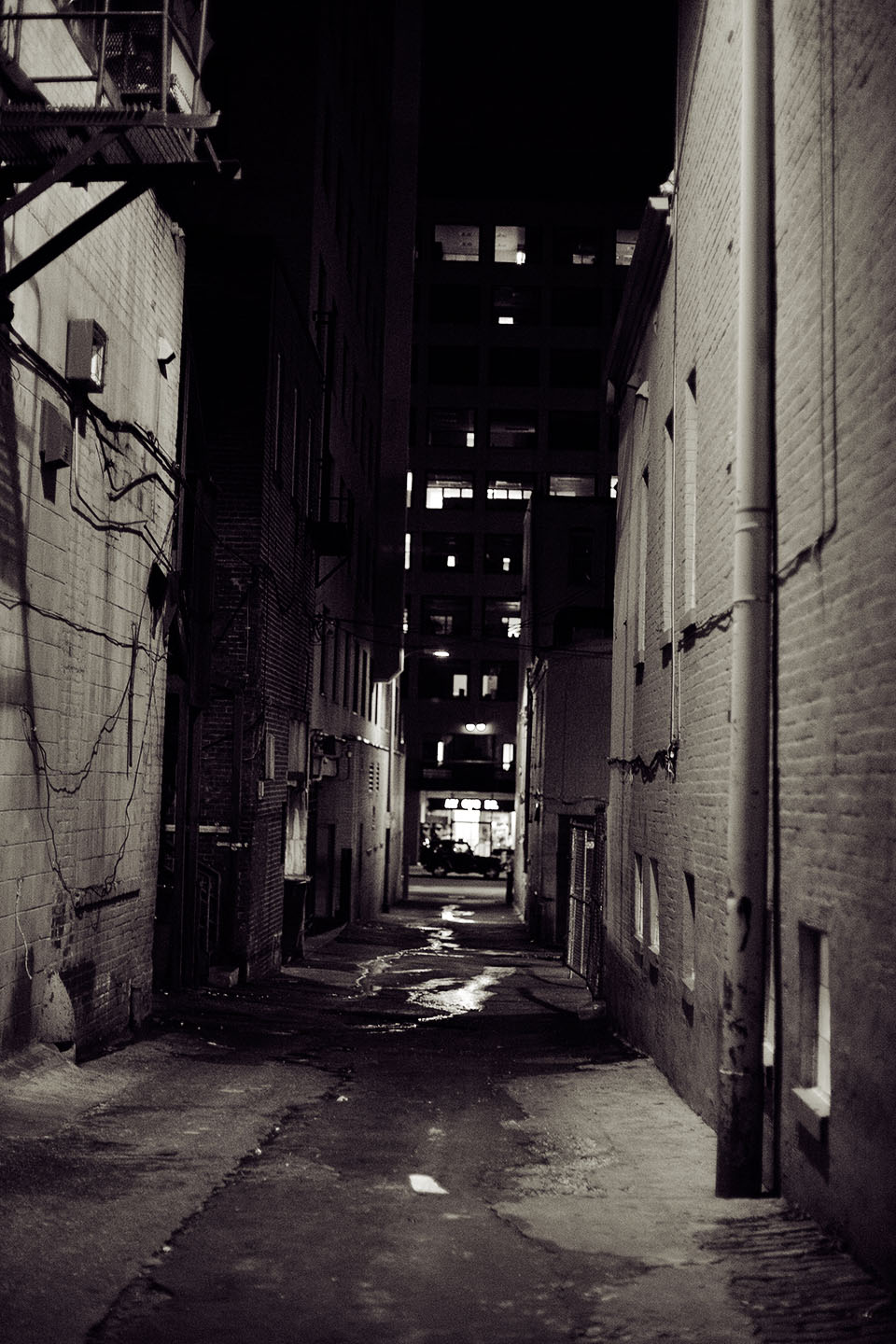 an alley with the building lights on, and buildings partially obscured in shadows