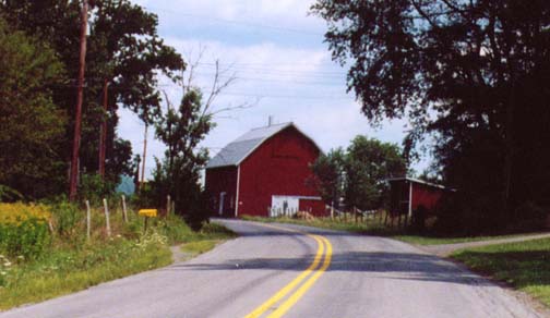 a red barn sits near a road and a grassy field