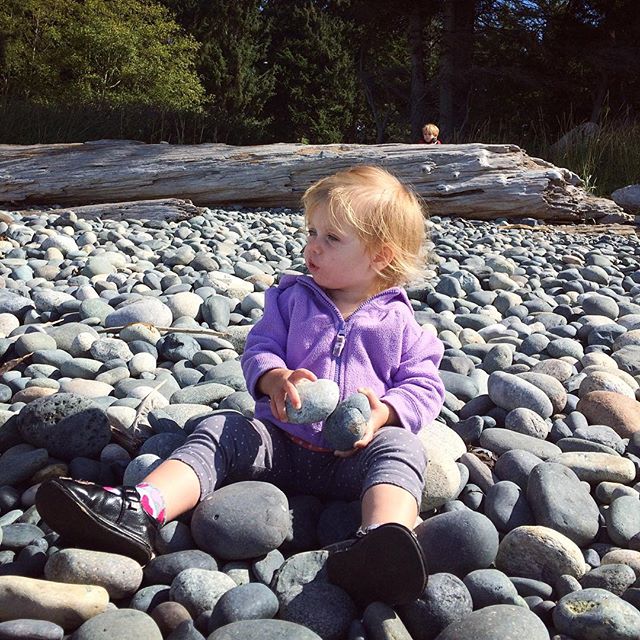 young child sitting on a rock on the beach with two rocks in their hands