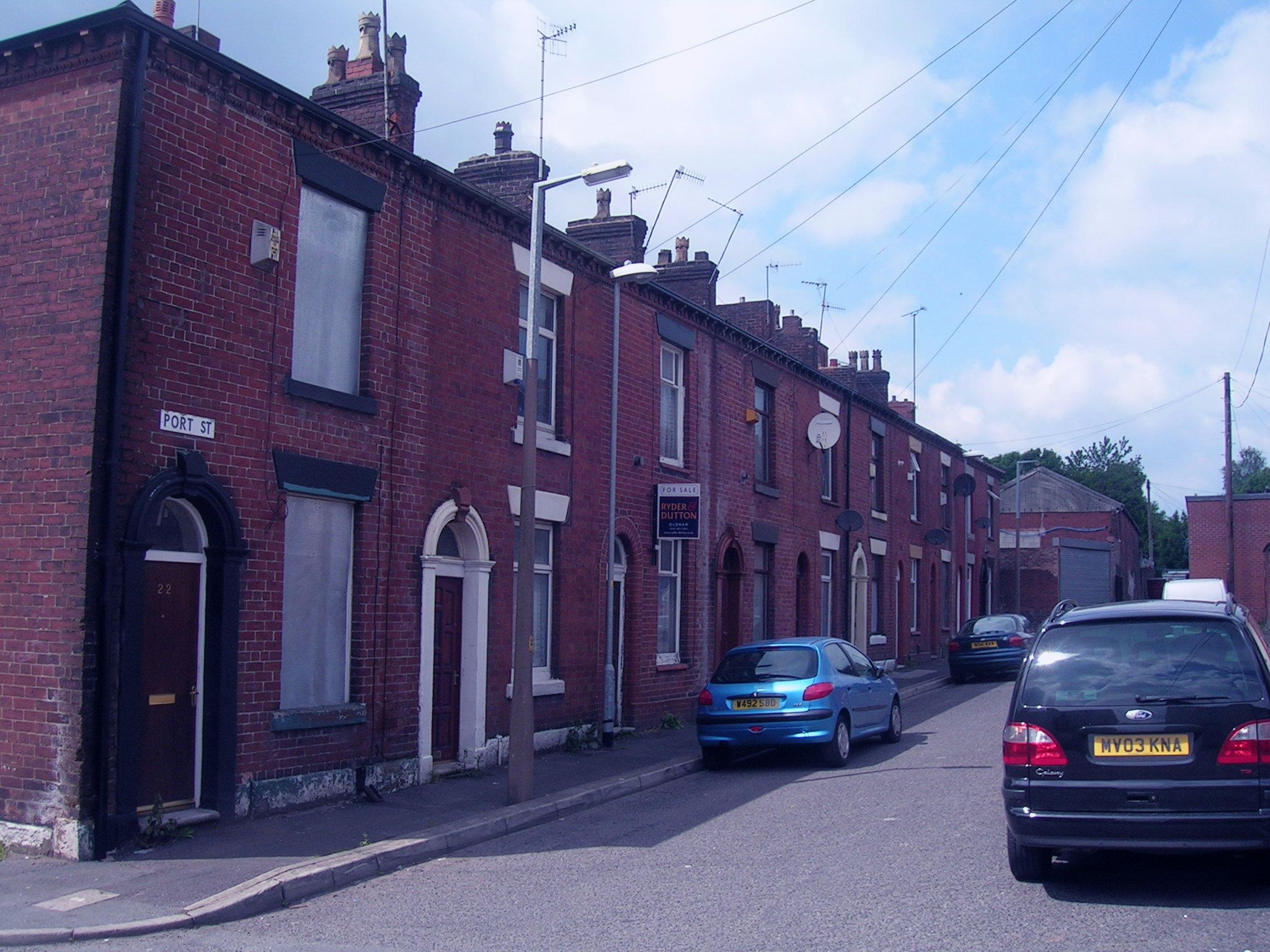 several cars parked along a brick street next to brick buildings