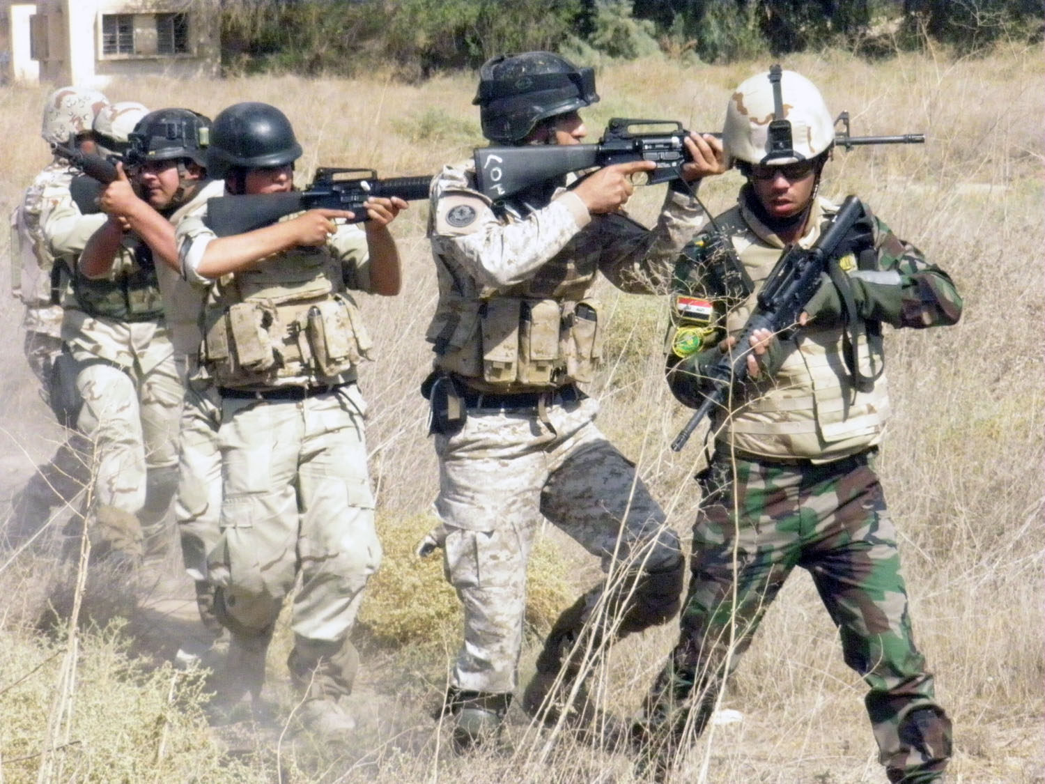 four men in camouflage gear, one holding a gun while the other has a gun