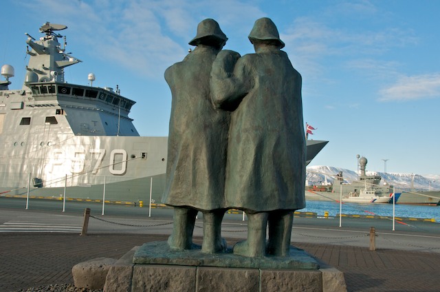 two sculptures are near a large battleship on a waterfront