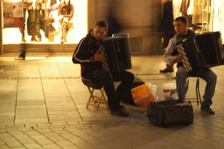 two men sitting down while one plays an accordion