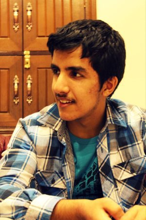 a young man with a mustache sitting on a couch in front of an old cabinet