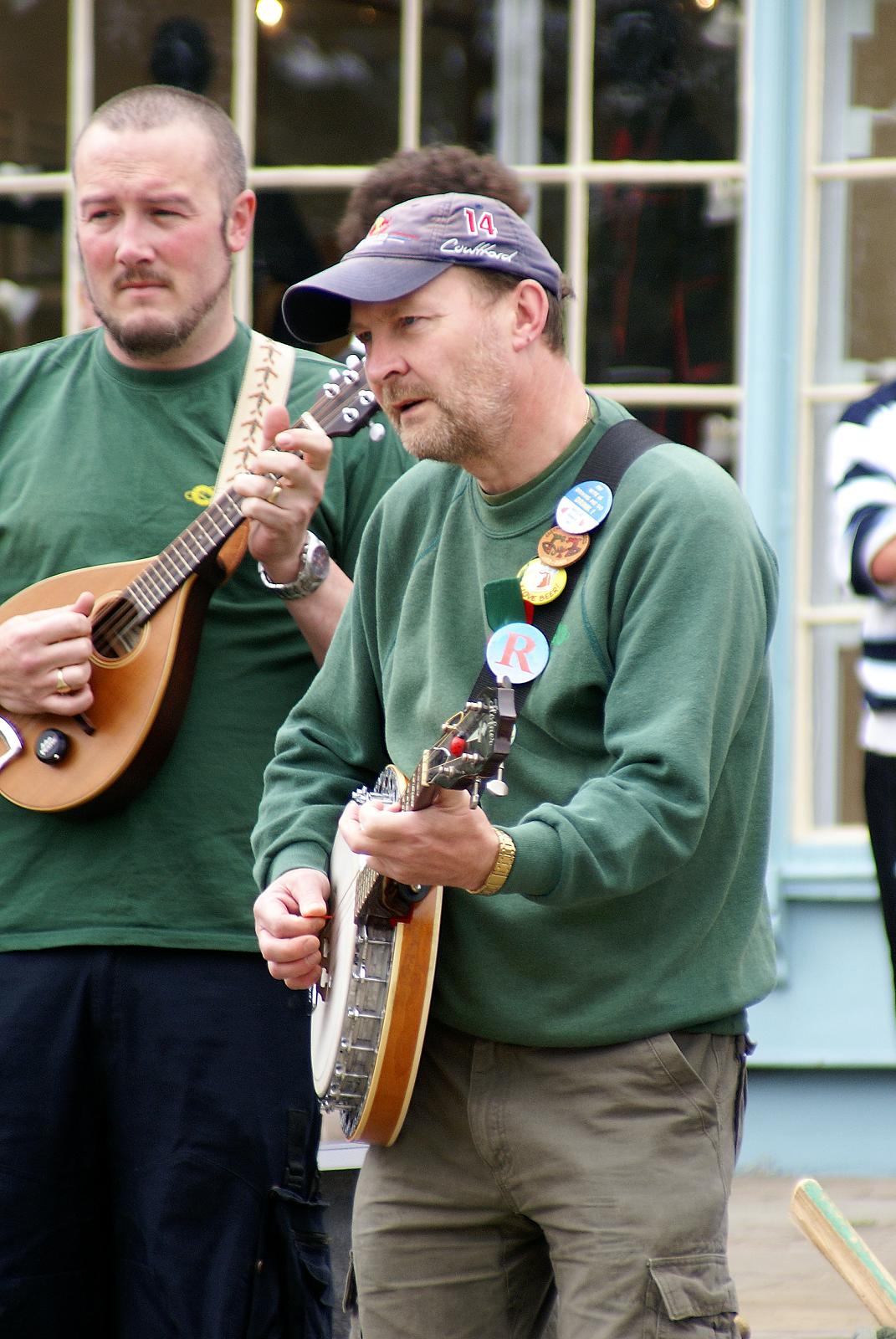 two men playing acoustic instruments near a building