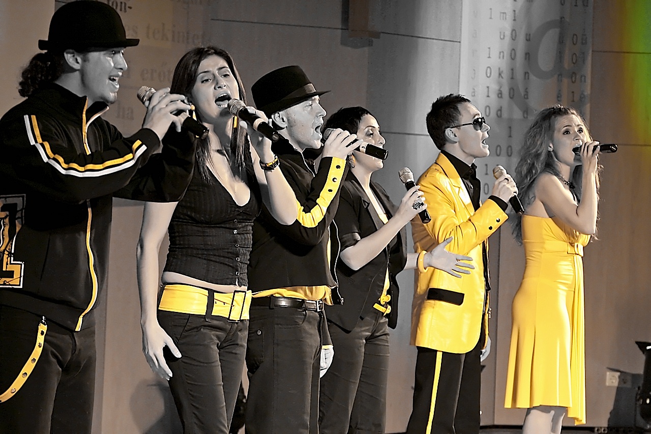 six people in black and yellow singing into microphones