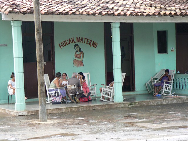 people sit outside of a turquoise building while one watches another