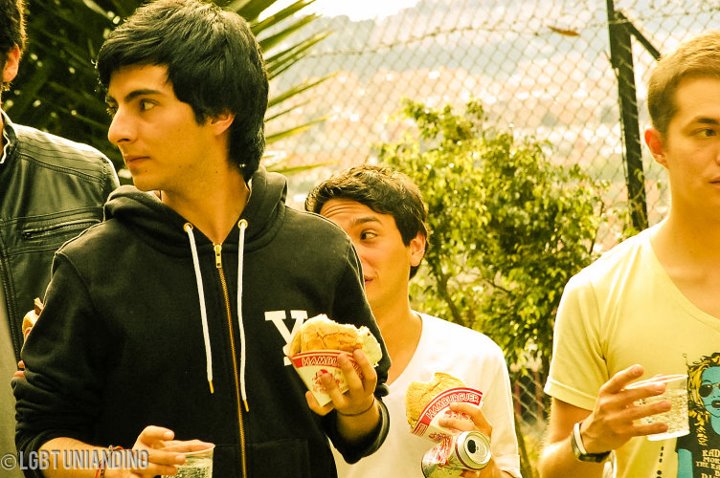 four guys, all wearing white shirts and one of them is holding a hamburger