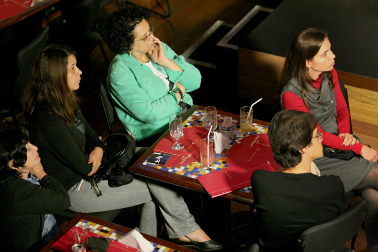 women sitting at tables and a lady standing talking to one another