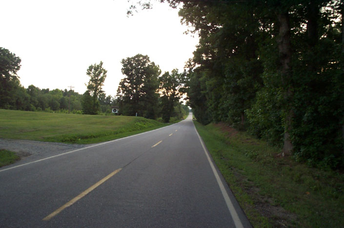 an empty street next to the woods and grass