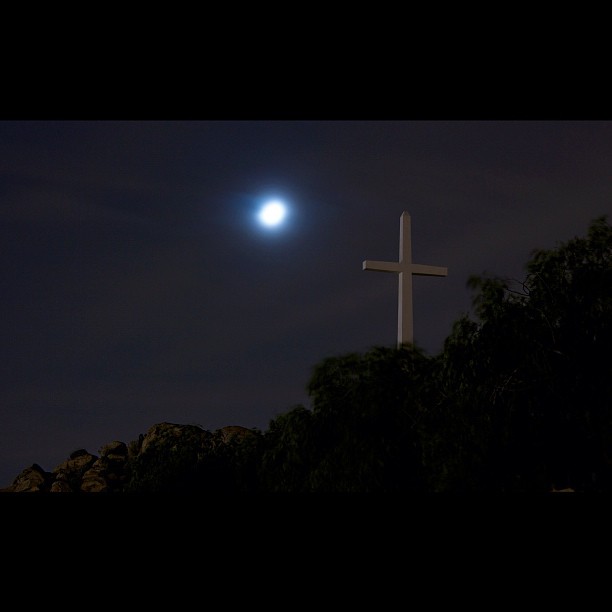 the moon is setting over a cross and hill