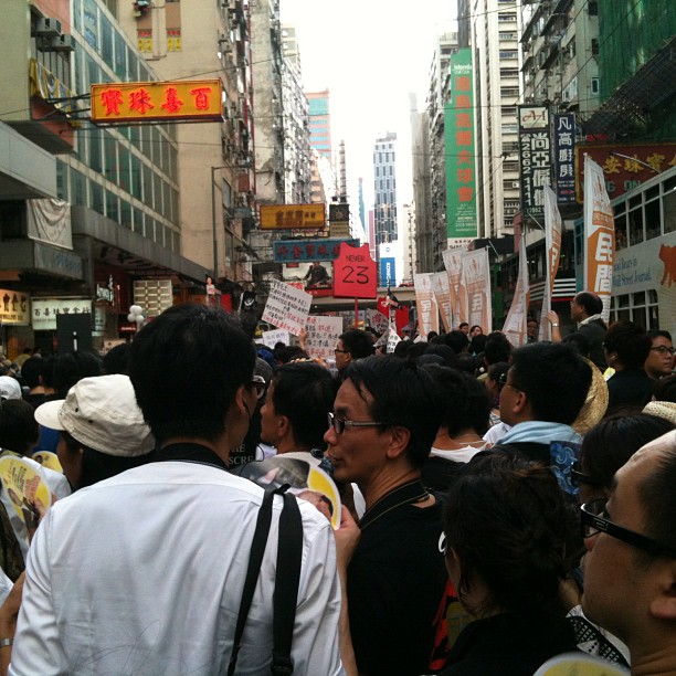 people walk down a busy crowded street carrying signs