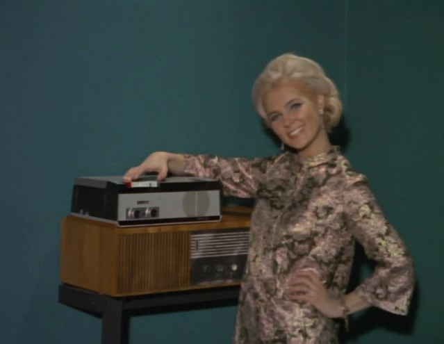a woman poses with an old radio in front of a blue wall