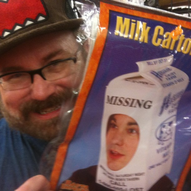 the man wearing glasses and a hat is holding up a package of milk