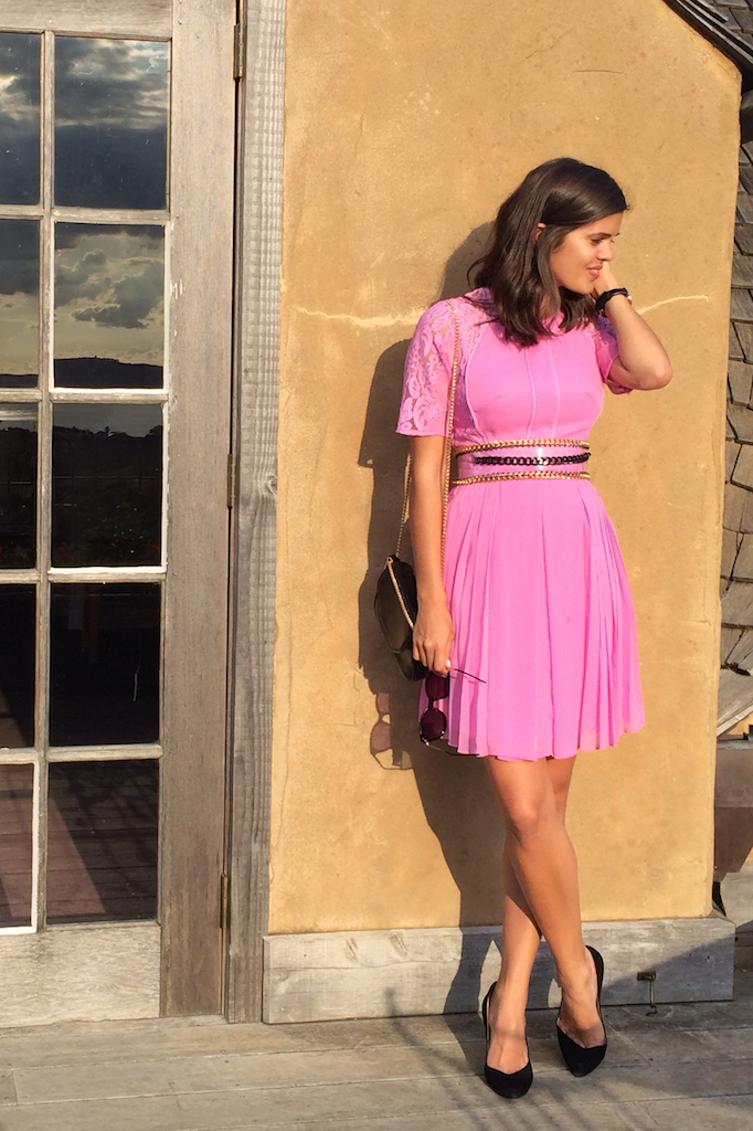 a woman in a pink dress leaning against a stucco wall