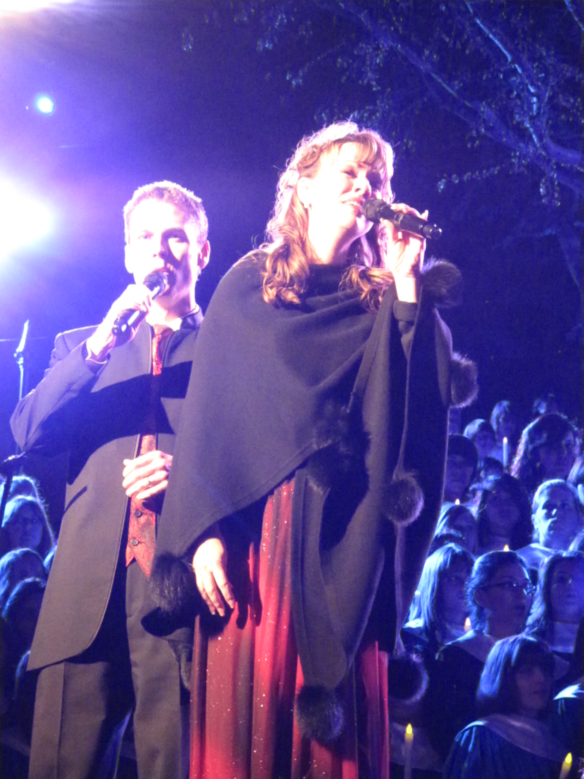 two people on stage one holding microphone while another holds her coat over her