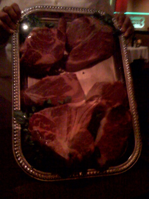 a woman holding an open metal tray filled with raw meat