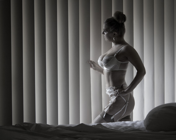 a woman wearing a  top standing in front of a bed