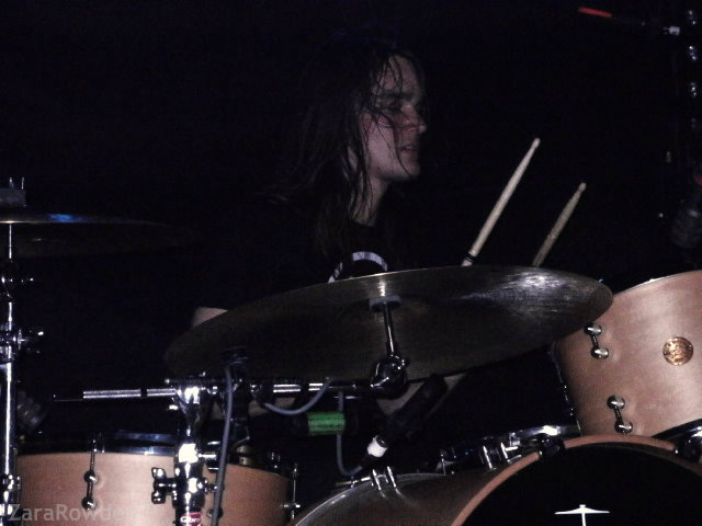 the drummer behind him with his kit playing drums