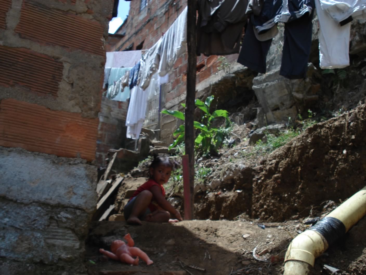 a little boy sitting on the ground in the dirt near some clothes