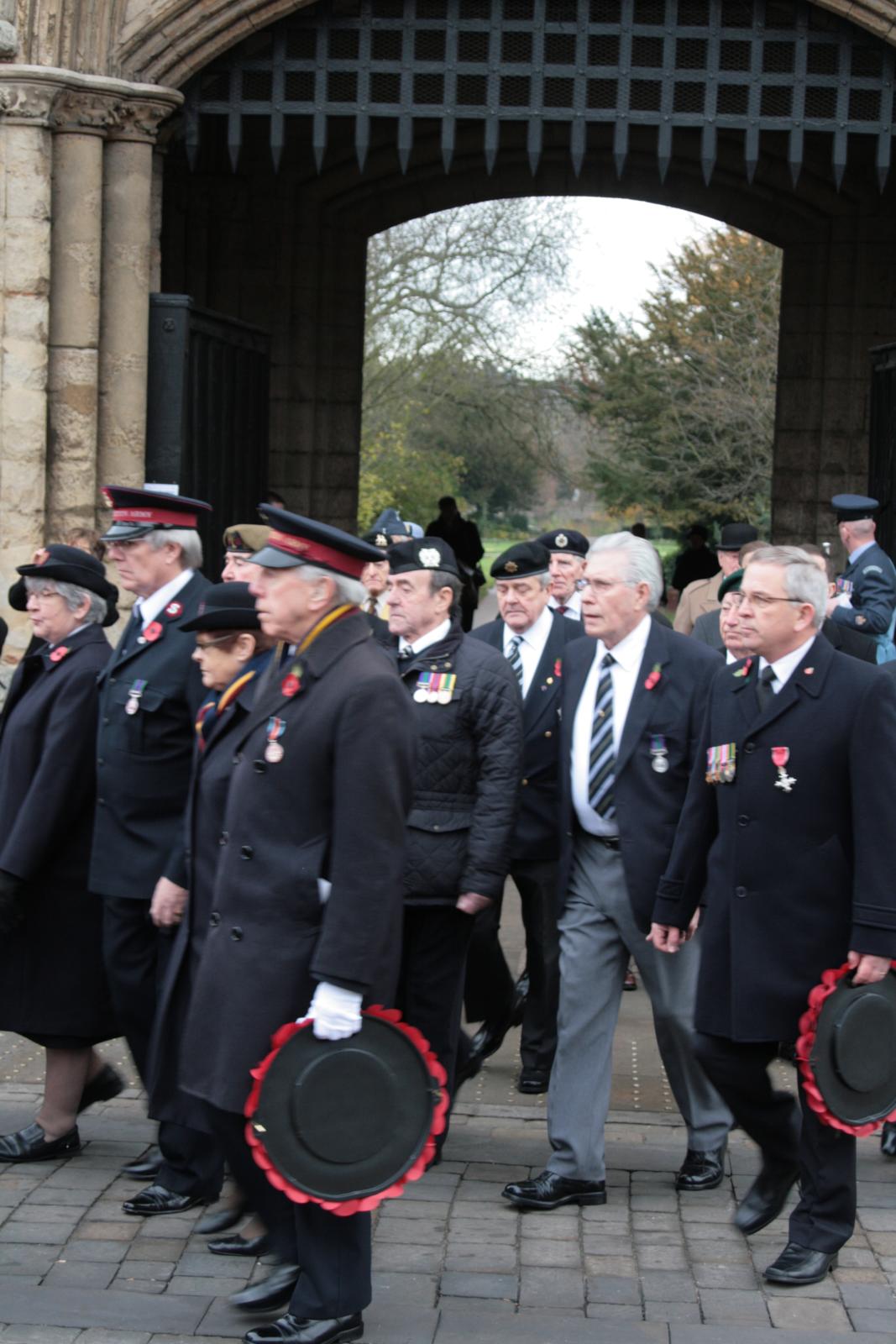 a group of people walk along the walkway with their hats in hand