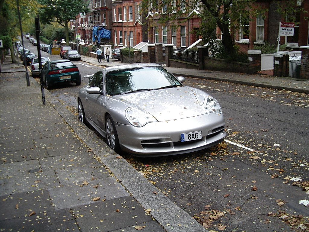 the silver car parked on the side of the street is next to a woman