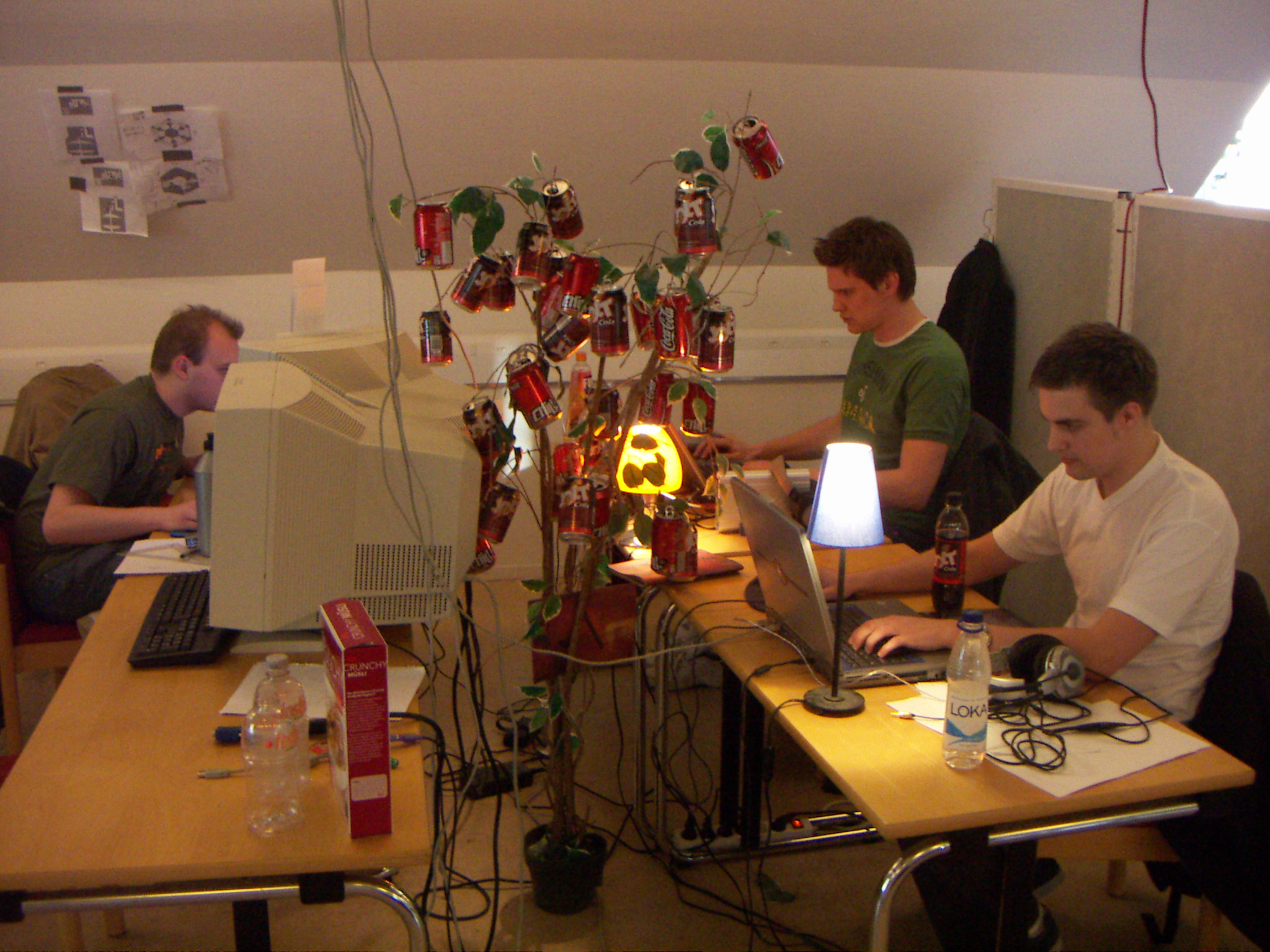 three men working on computers at desks with christmas lights on them