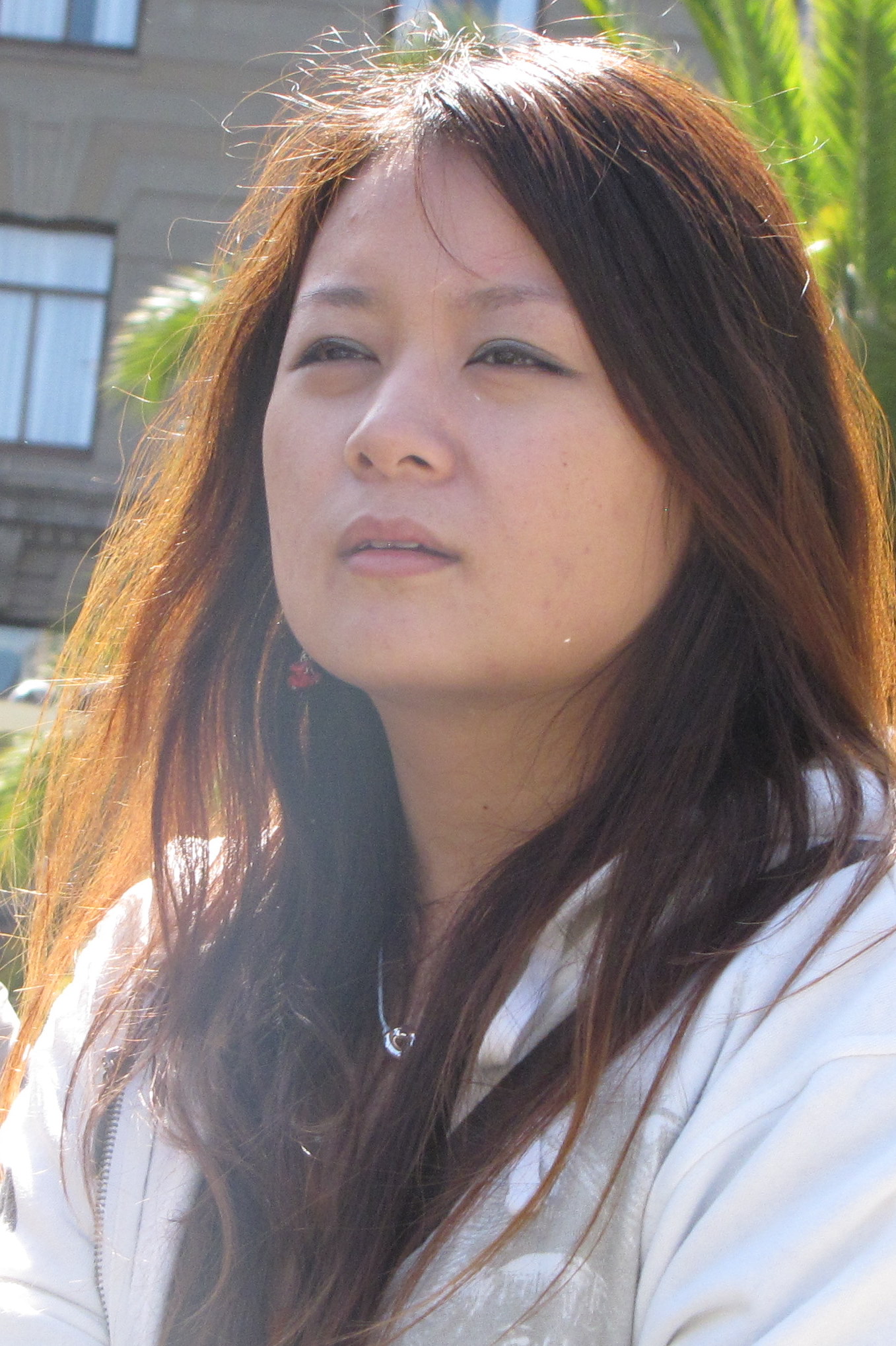 an asian woman wearing a white shirt and earrings looking into the distance