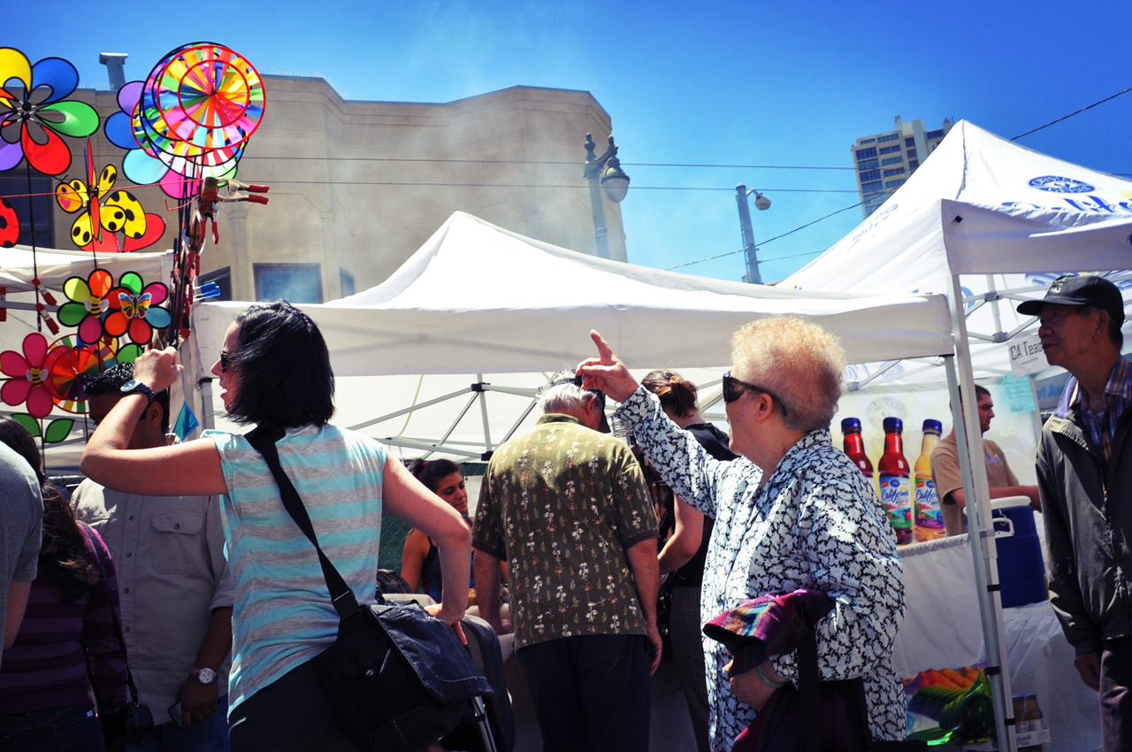 people at an outdoor event in front of tents with umbrellas